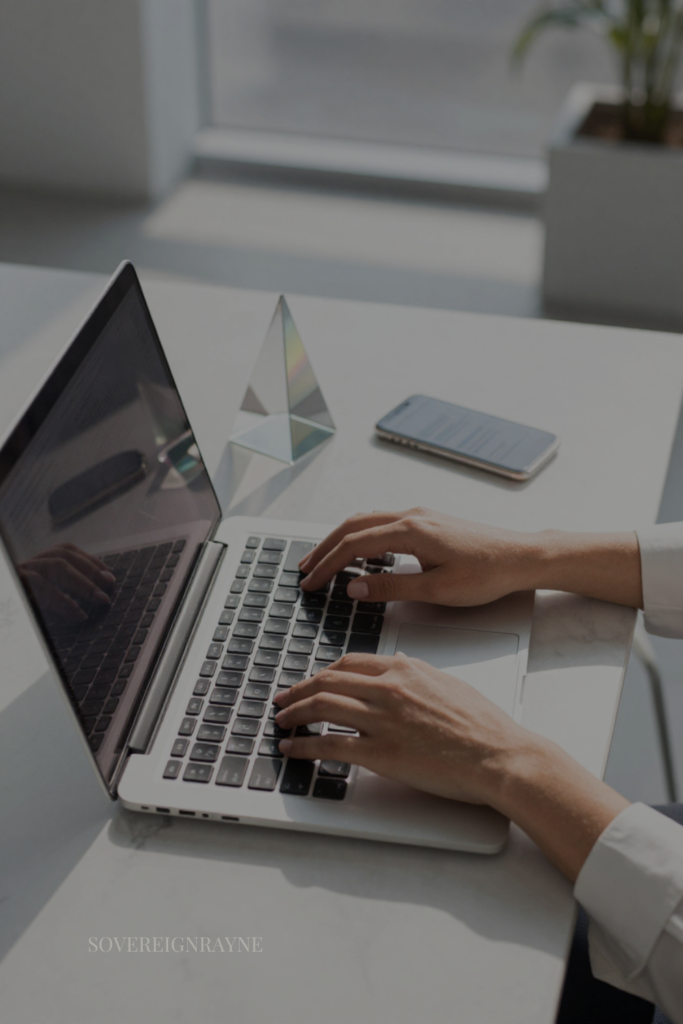 Close-up of a professional woman working on a laptop at a marble desk next to a geometric prism, illustrating grounded spiritual growth for high-achievers.
